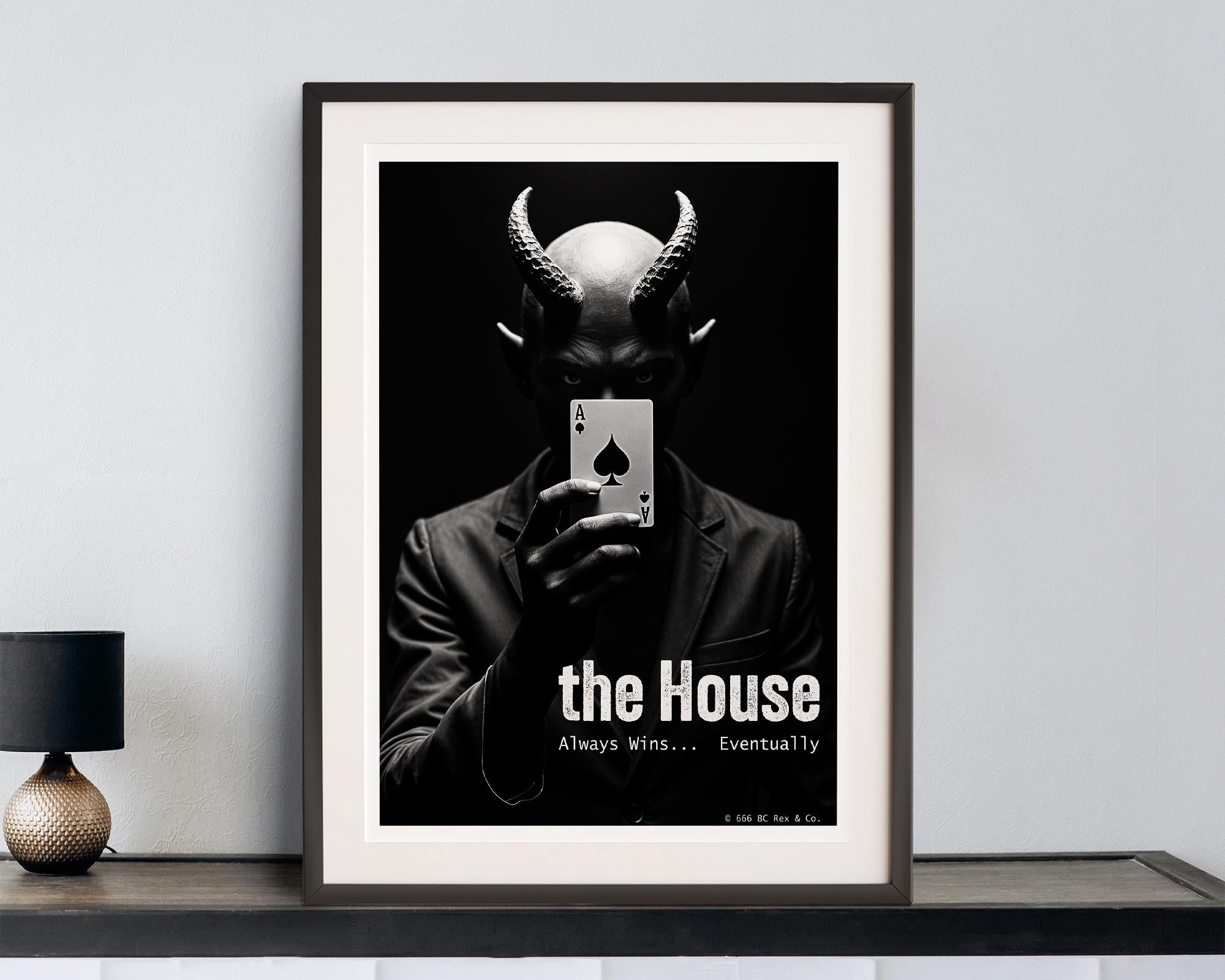 Framed poster with a black and white design of a devil holding a card, displayed on a shelf.