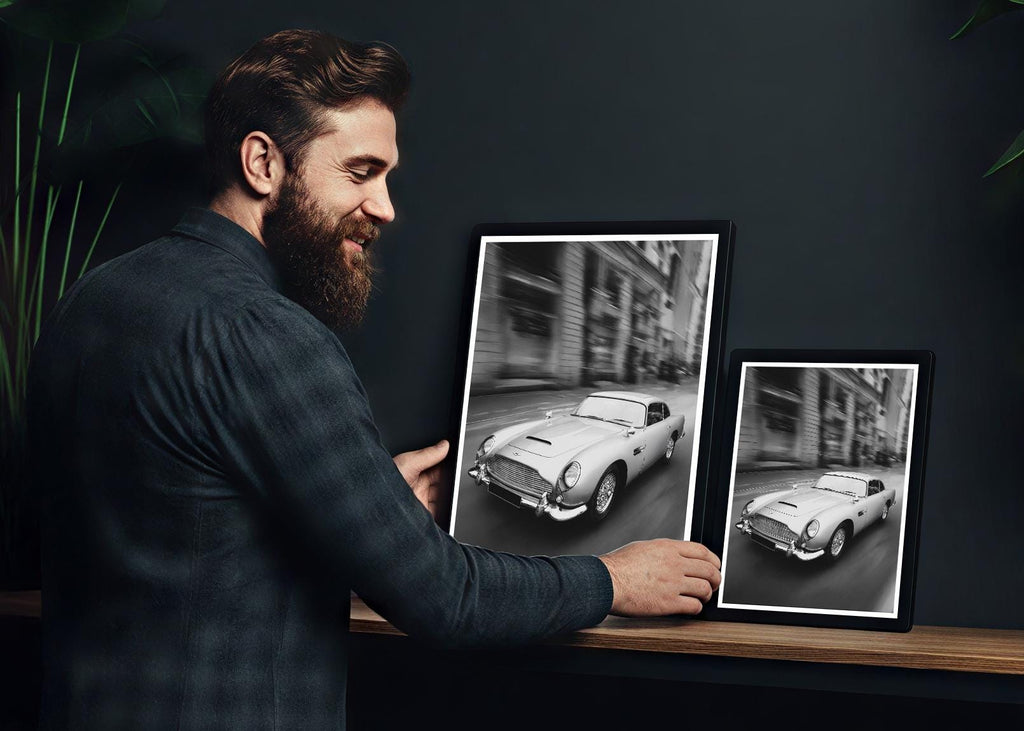 Man looking at framed black and white photos of classic cars on a shelf.