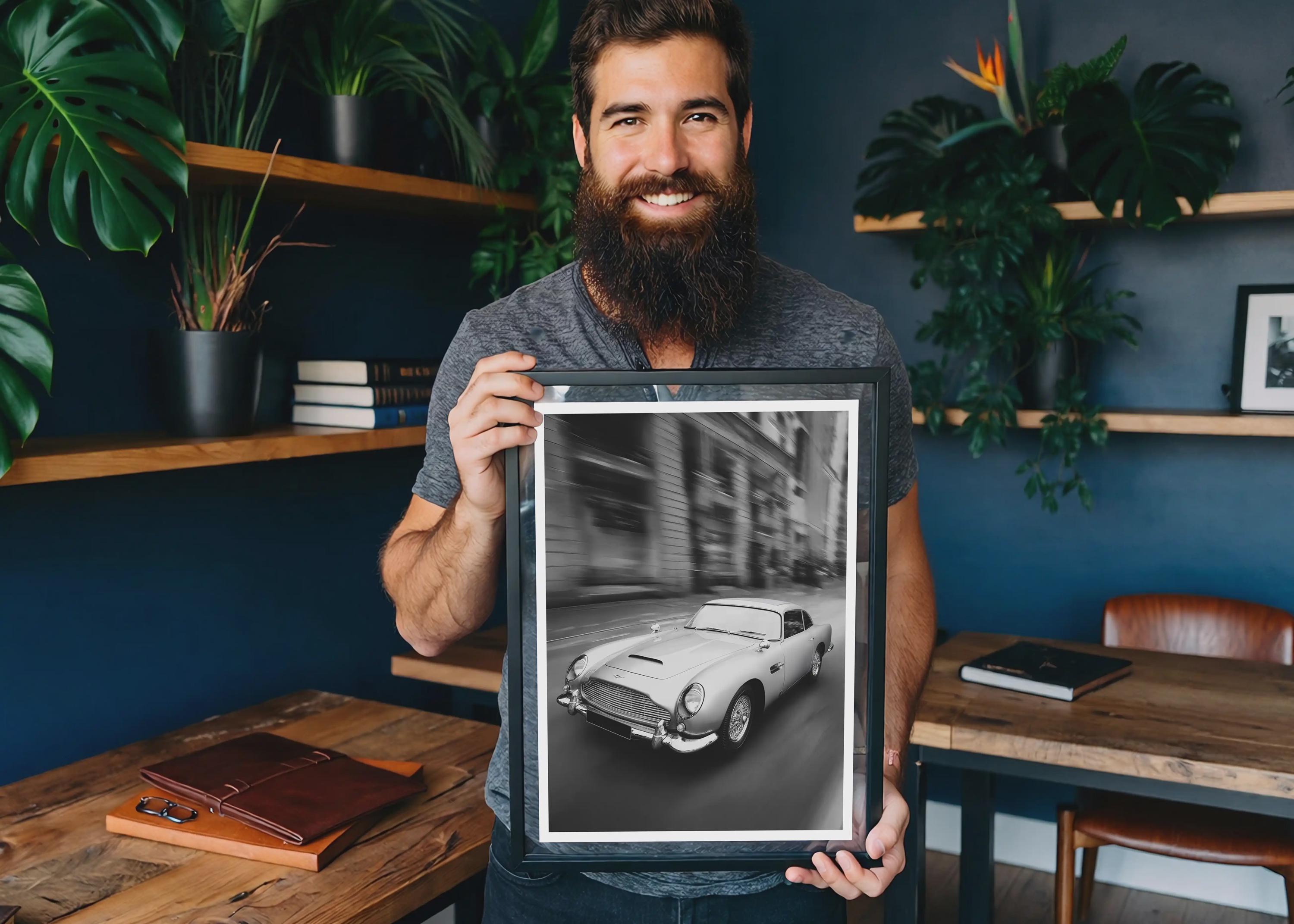 Man holding a framed black and white photo of a vintage car in a room with plants and wooden furniture.