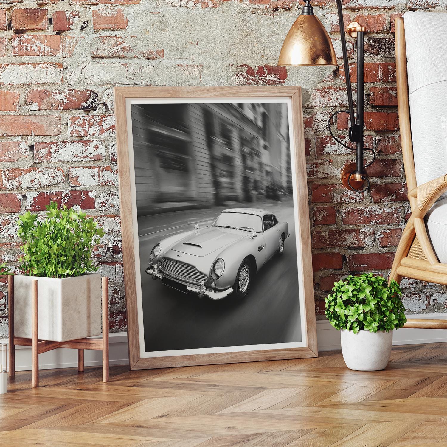 Framed black and white photo of a vintage car on a brick wall with plants and a lamp.