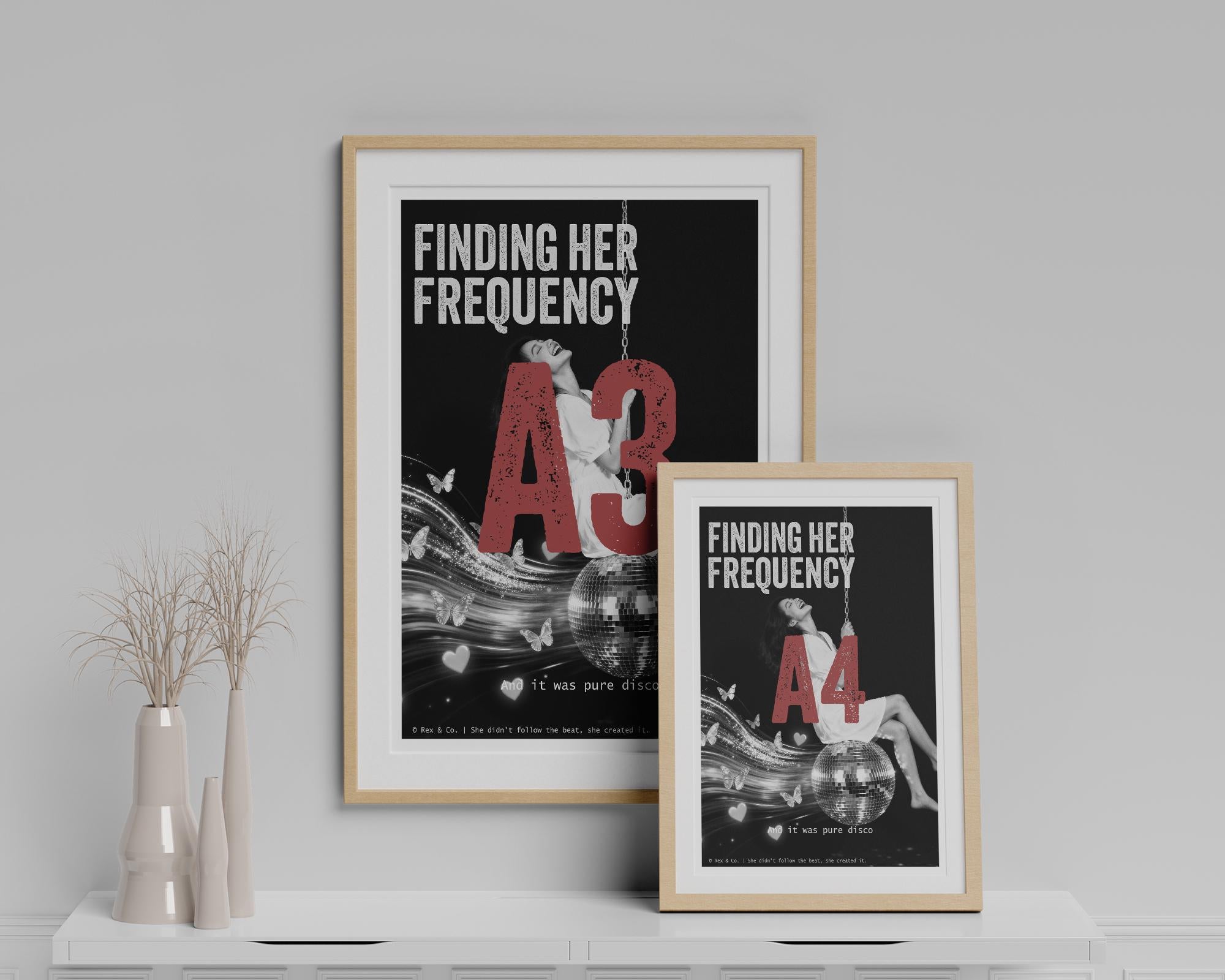 Two framed posters titled 'Finding Her Frequency A3' and 'Finding Her Frequency A4' on a white shelf against a gray wall.