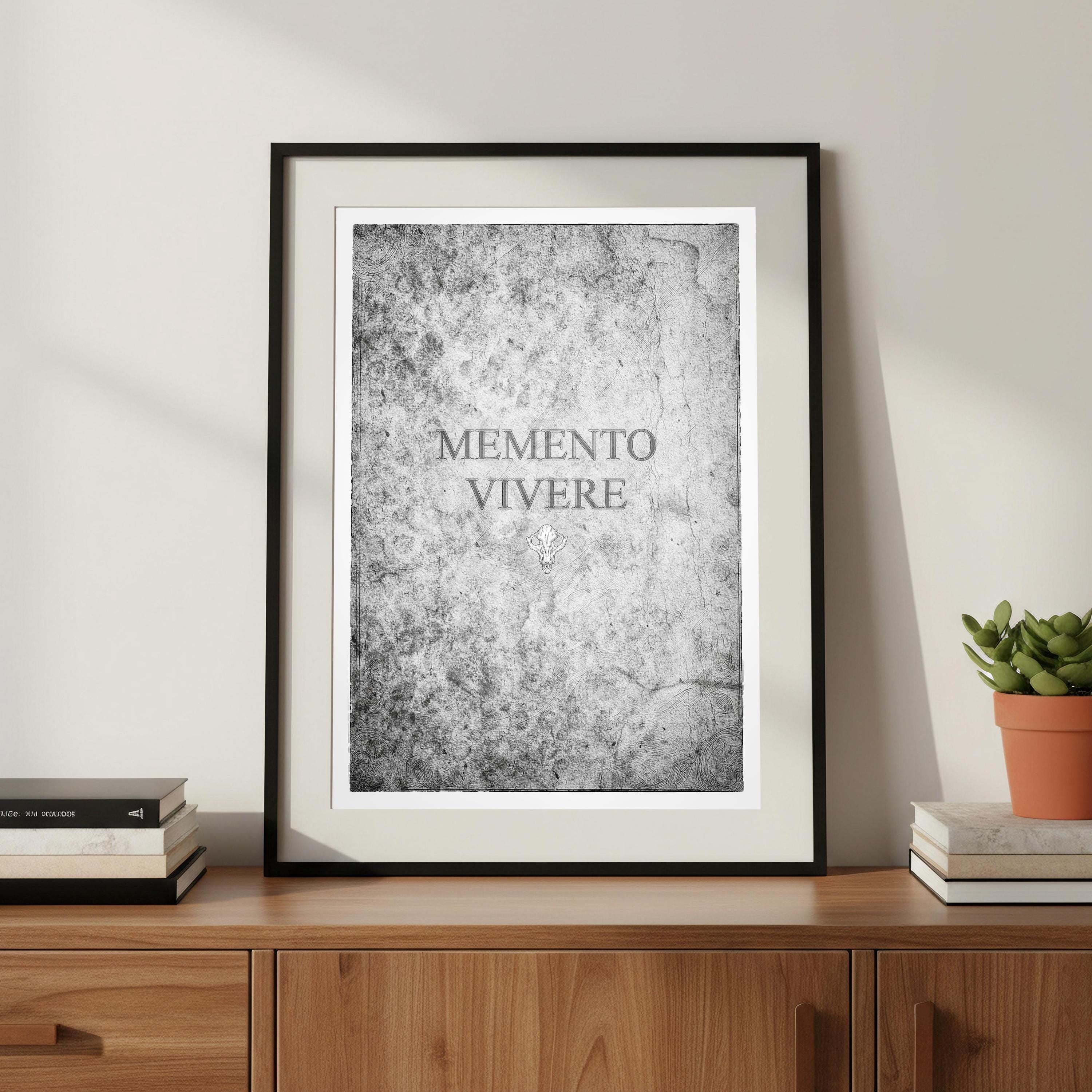 Framed print with 'MEMENTO VIVERE' text on a wooden surface with books and a plant.