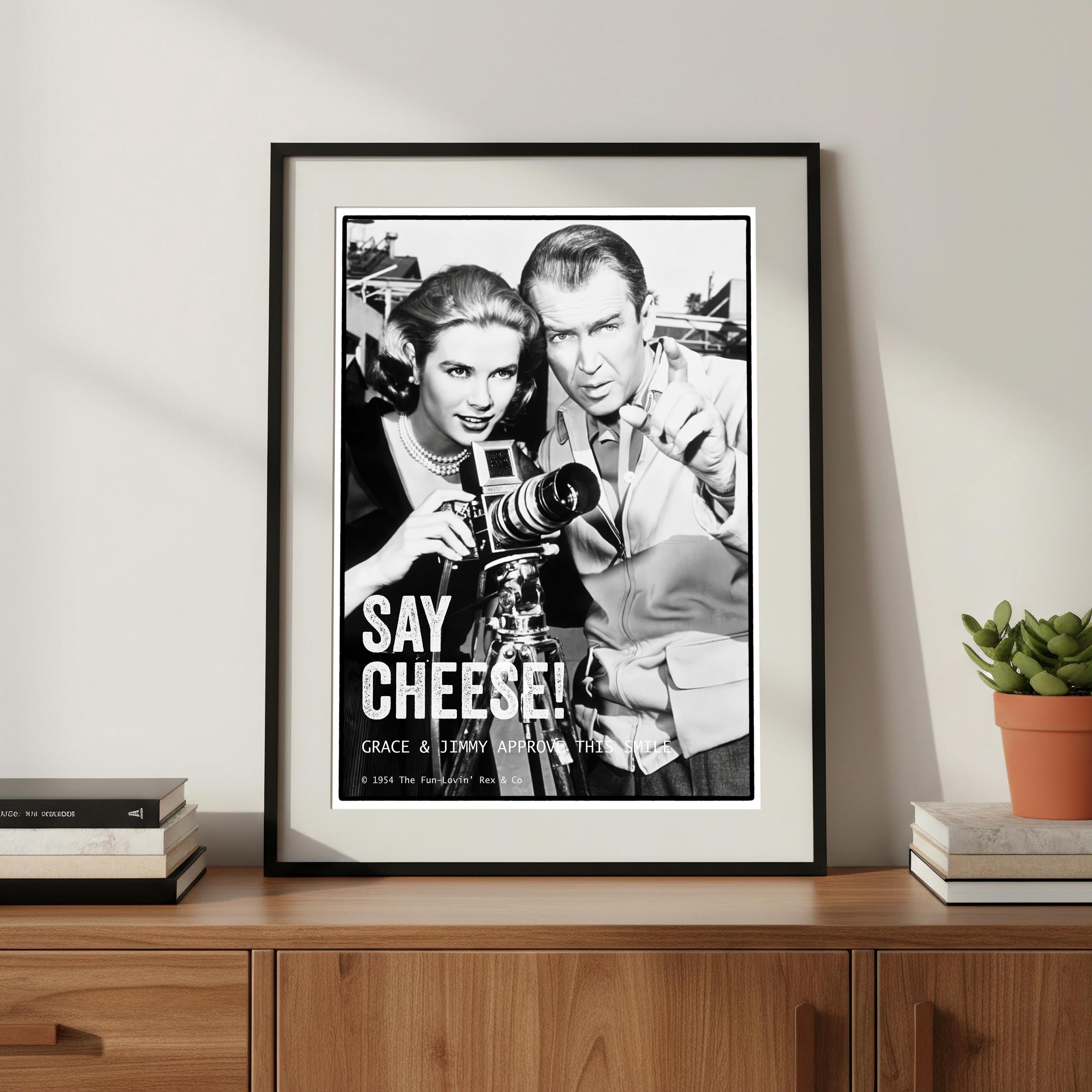 Framed black and white poster of Grace Kelly and James Stewart with a camera on a wooden shelf.