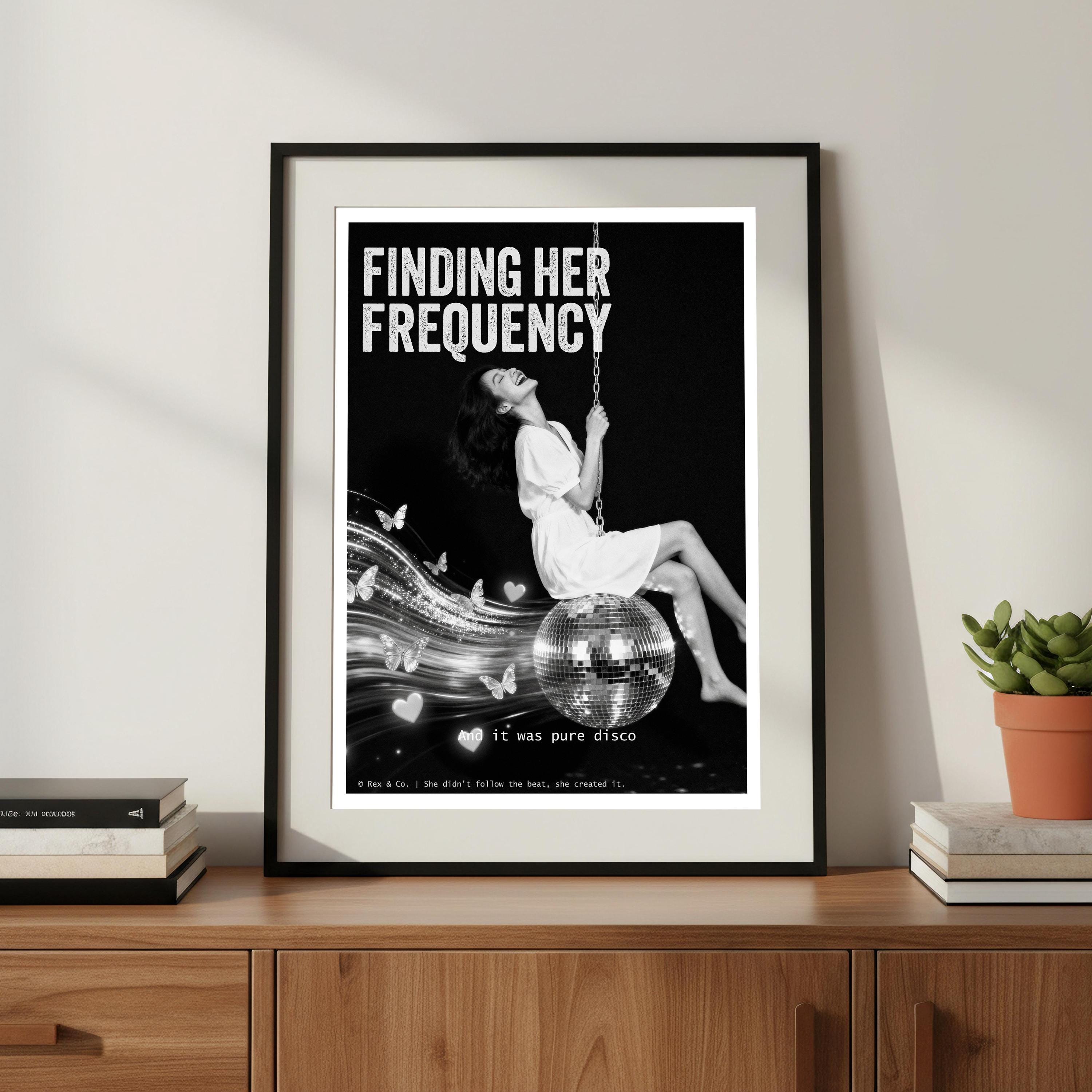 Framed poster with 'Finding Her Frequency' text and a woman on a swing, displayed on a wooden shelf.