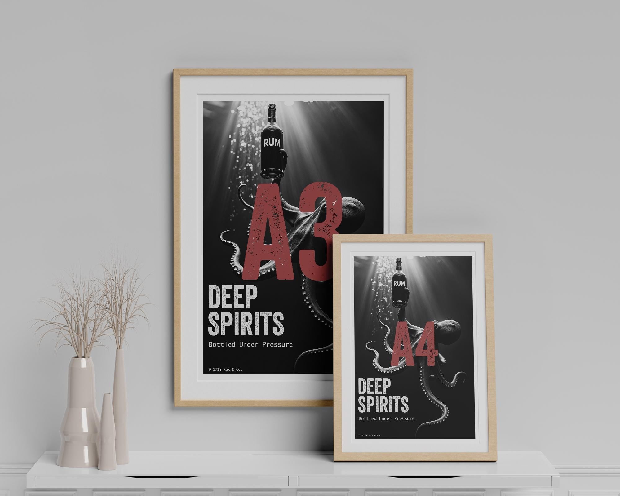 Two framed posters titled 'A3 Deep Spirits' and 'A4 Deep Spirits' on a shelf with a gray wall background.