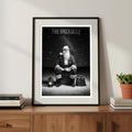 Framed poster of Santa titled 'The Overseer' on a wooden shelf with books and a plant.