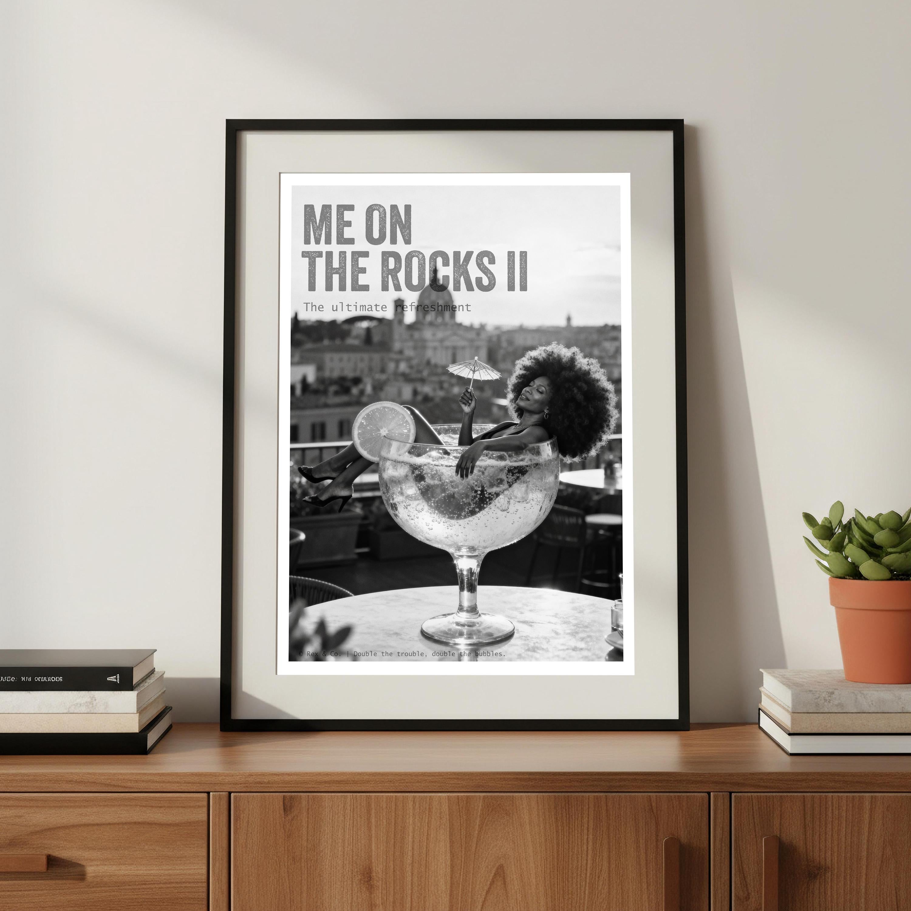 Framed artwork of a woman in a large glass with text 'Me on the Rocks II' on a wooden surface.