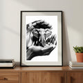 Framed artwork of hands holding a small elephant on a wooden surface with books and a plant.