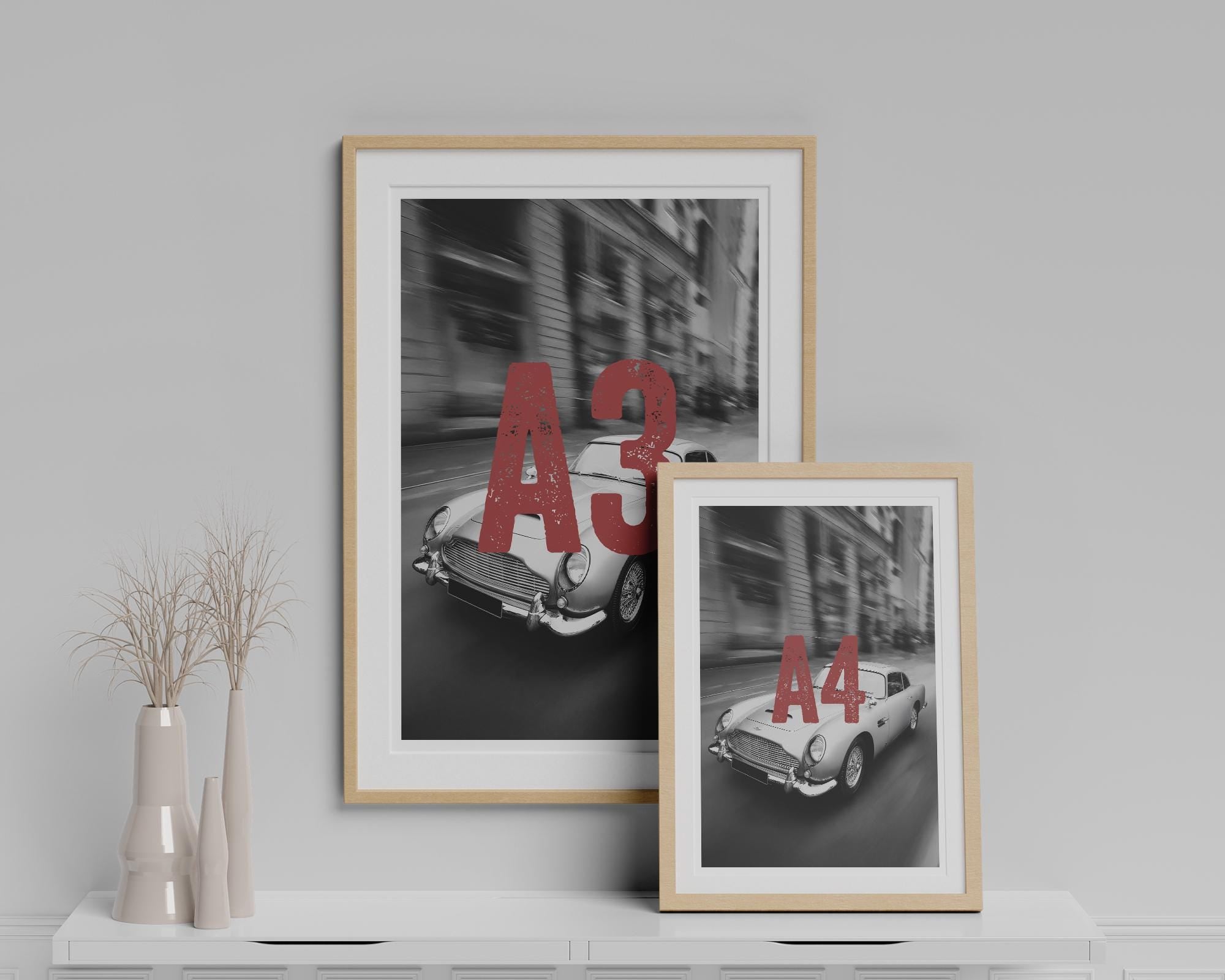 Two framed prints of vintage cars with numbers on a gray wall.