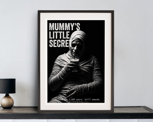 Framed poster with a mummy holding a cocktail and text 'Mummy's Little Secret' on a white wall.