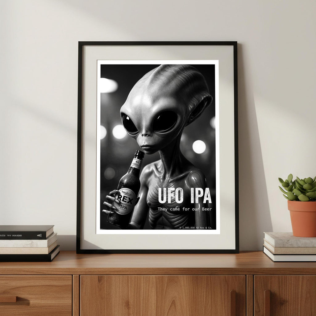 Framed poster of an alien holding a beer bottle with 'UFO IPA' text on a wooden surface.