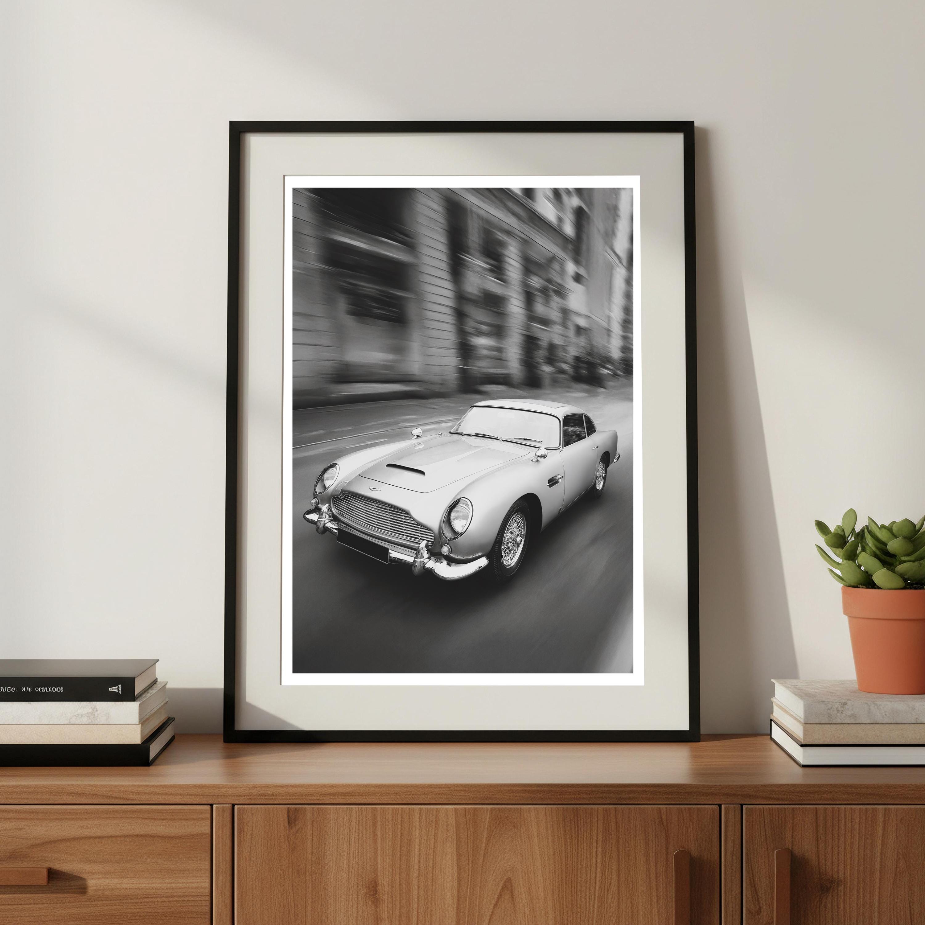 Framed black and white print of a classic car on a wooden shelf with books and a plant.