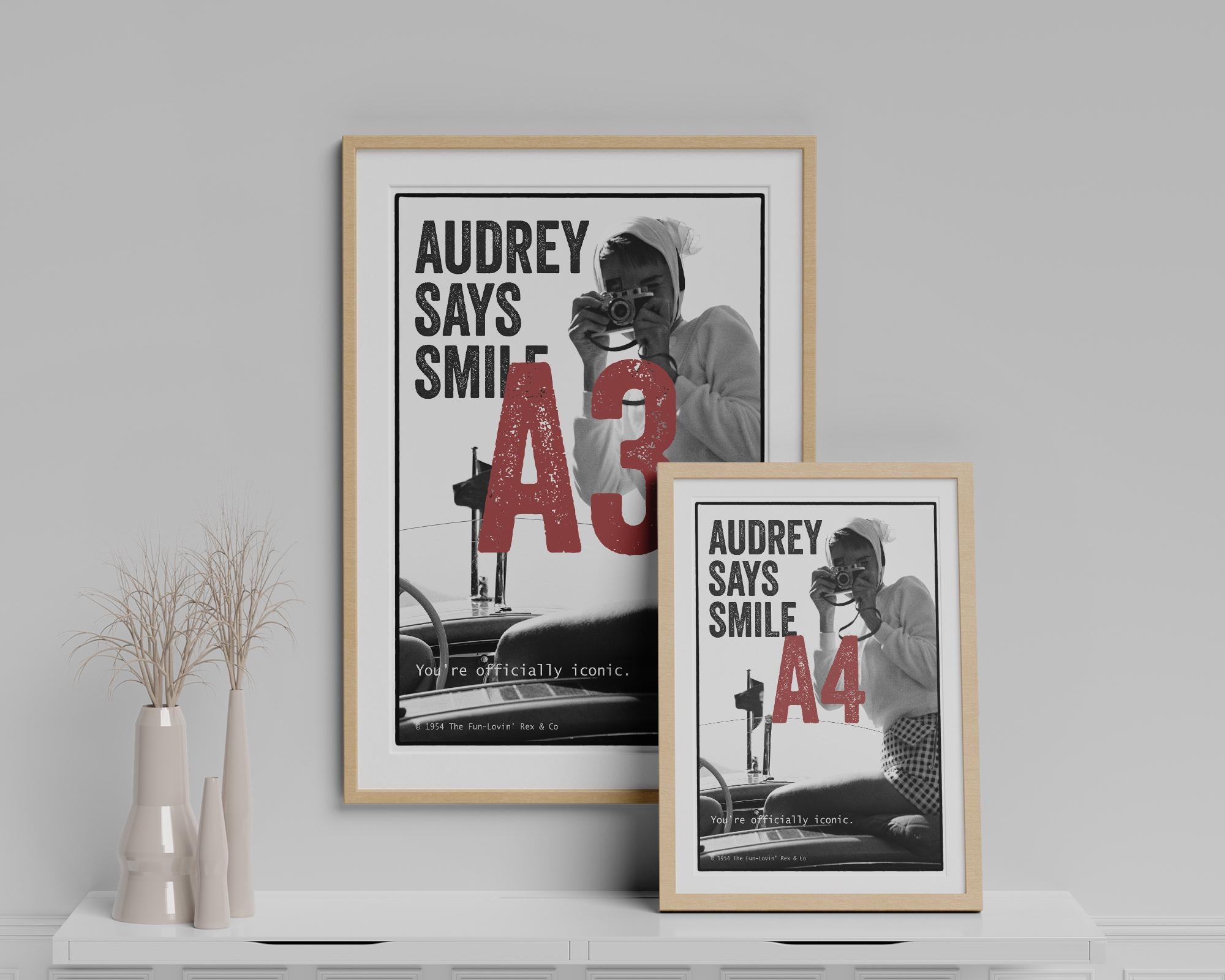Two framed posters of Audrey Hepburn on a shelf with a neutral background